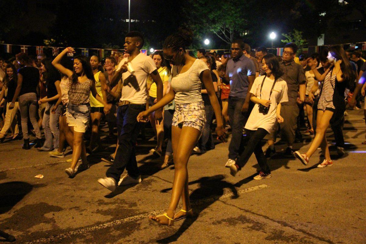 Students from various ages and backgrounds excitedly perform the line dance to "Cupid Shuffle" outside the I-House at Beyond the Borders.
