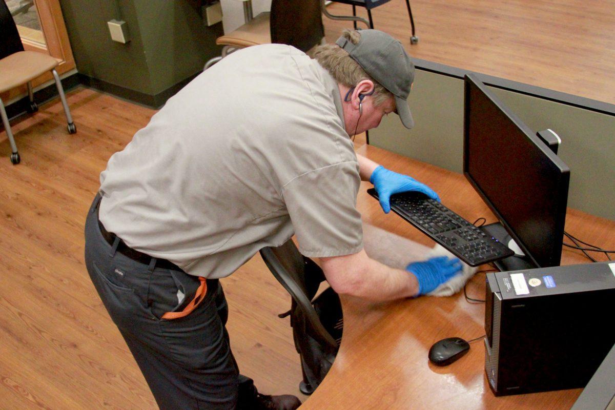 Campus worker David Collins cleans under a computer keyboard during his eight-hour night shift in the Commons of Hodges Library on Monday.