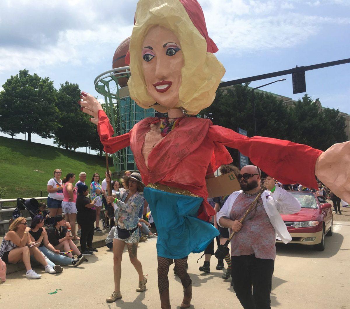 A large Dolly Parton puppet waves to parade spectators. 