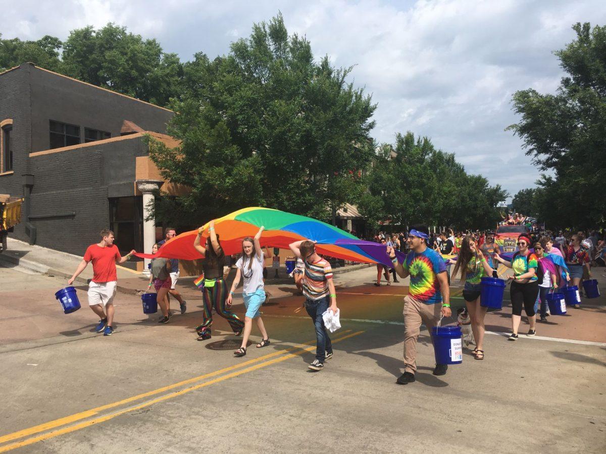 A large flag is carried across the road by many people holding its edges. 