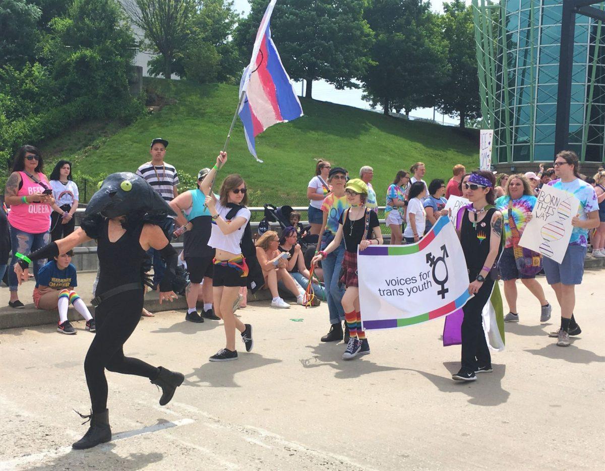 A parade performer dances ahead of "Voices for Trans Youth", dressed as a raven. 
