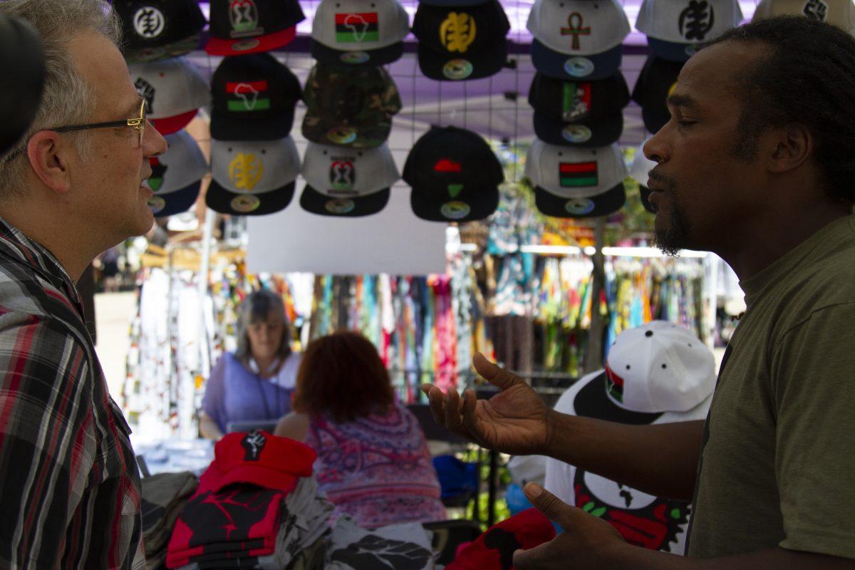 Vendor Wisdom Jzar discusses the meaning behind the symbols on his merchandise to a customer. 