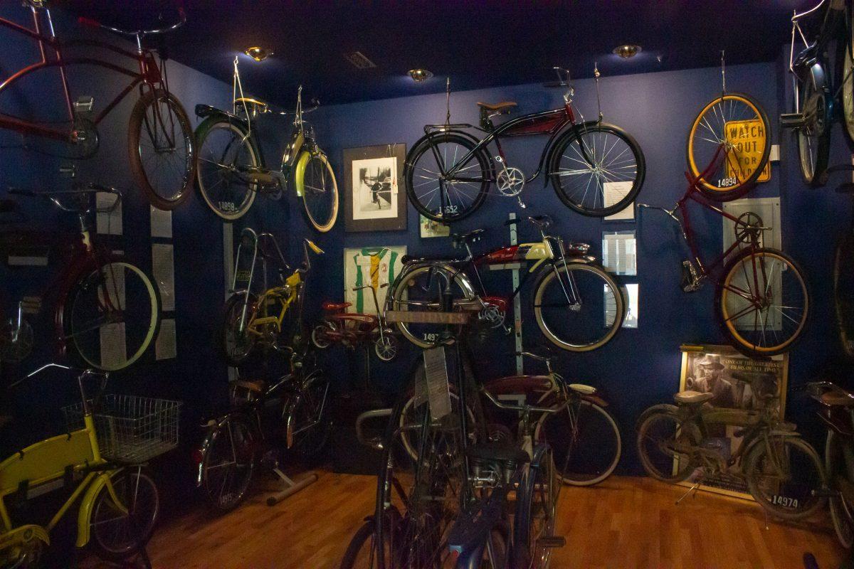 The inside of the Little Congress Bicycle Museum. Bicycles hang on three of the four walls, each one with a nameplate and description beside it.
