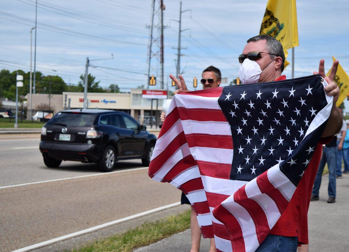 A protester holds up an American flag along Kingston Pike during the Knoxville Freedom Rally outside the closed West Town Mall on Sunday, April 19, 2020.