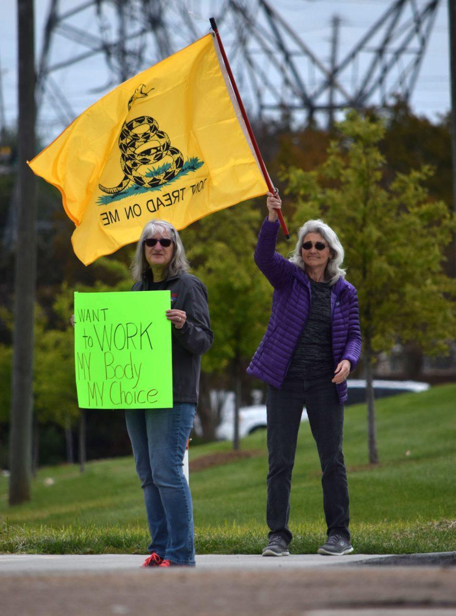Two protesters stand on the corner of Morrell Road and Kingston Pike outside West Town Mall holding a sign and "Don't Tread on Me" flag during the Knoxville Freedom Rally on Sunday, April 19, 2020. The protest is one of seven in major cities across Tennessee rallying against Governor Bill Lee's mandatory shutdown of nonessential businesses because of the coronavirus outbreak.