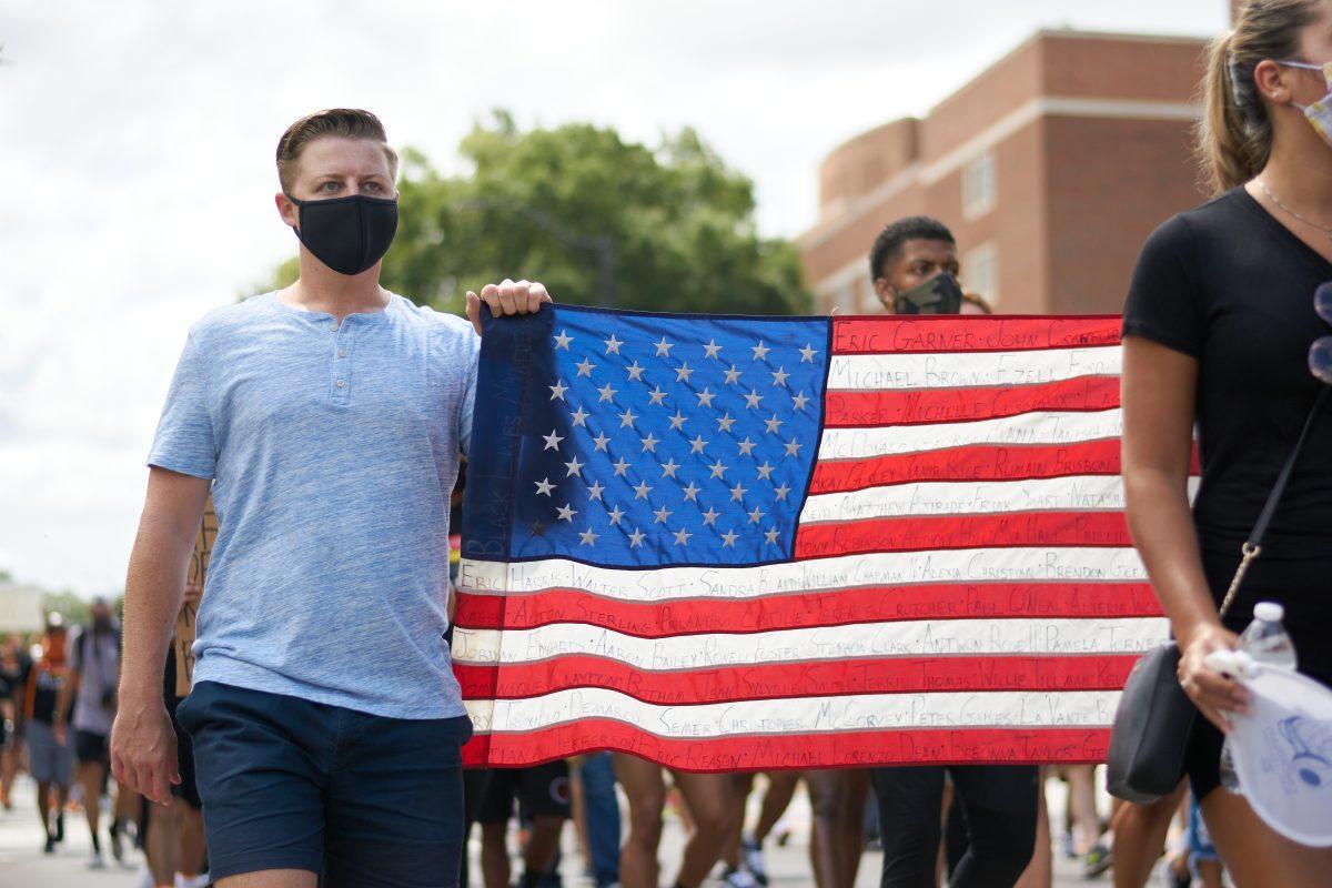 A supporter marches down Volunteer Boulevard holding an American flag, inscribed with the names of victims of racial violence, during the BLM March on August 29, 2020.