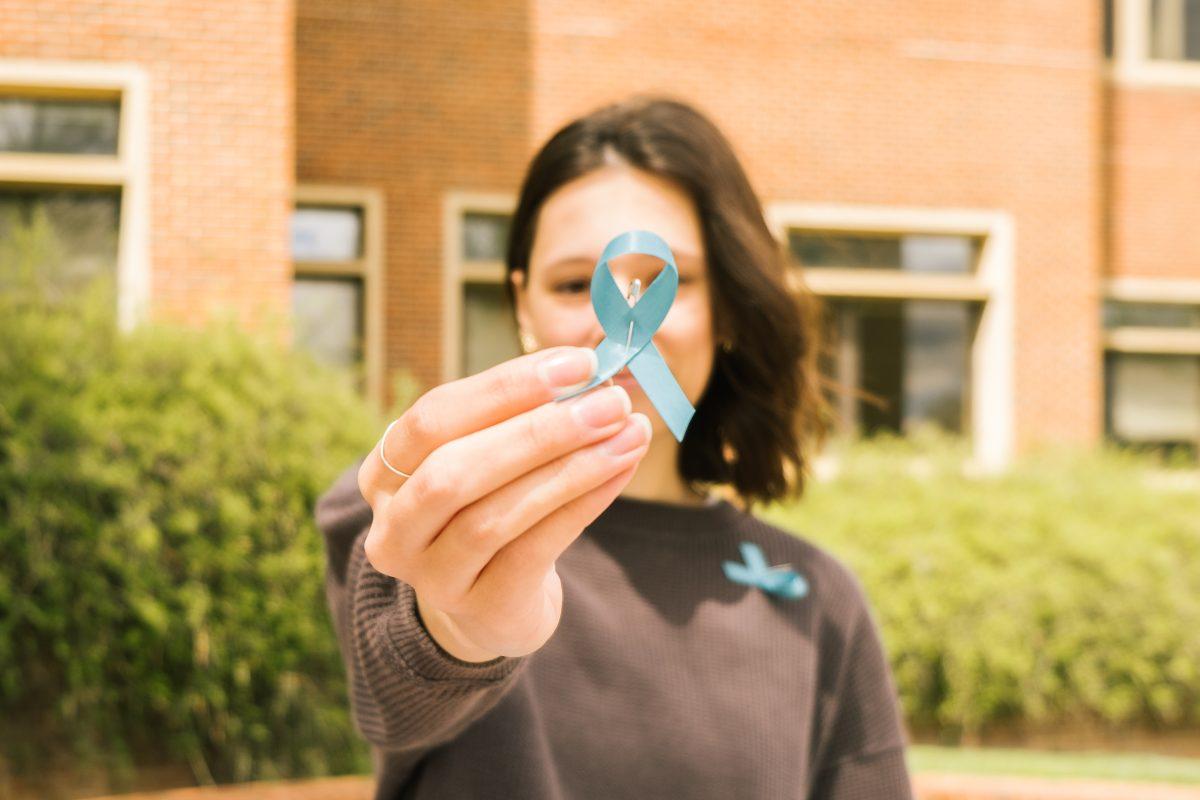 UT student holds up a blue ribbon representing Sexual Assault Awareness Month. Thursday April 7, 2022.