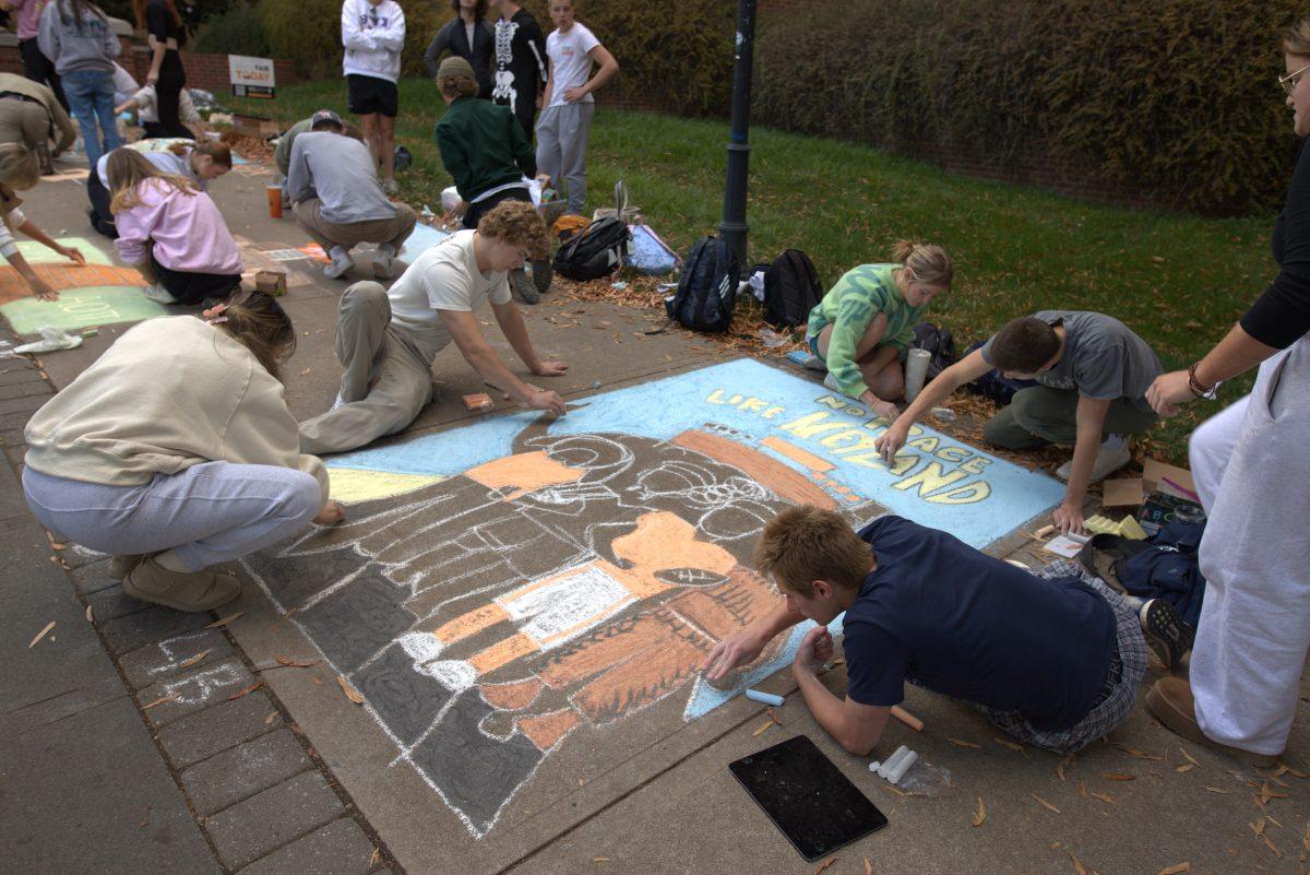Students work together to create a chalk illustration for Homecoming on Ped Walkway on Oct. 31, 2023.