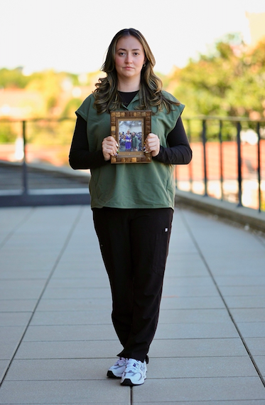 UT nursing and graduate student Klara Dolin stands tall in her nursing scrubs holding a framed photo of Conor.
